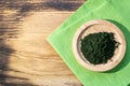 Bamboo plate with green chlorella powder on green linnen napkin on wooden background in sunny day, top view, copy space