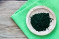 Bamboo plate with green chlorella powder on green linnen napkin on wooden background, top view, copy space