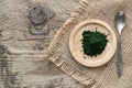 Bamboo plate with green chlorella powder with vintage spoon on canvas linnen napkin on wooden background, top view