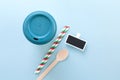 Bamboo reusable takeaway cup with lid on with paper straws, wooden spoon and blank blackboard tag, flat lay on blue background Royalty Free Stock Photo