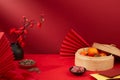 A bamboo steamer containing tangerines, a plate of sunflower seeds, a plate of salted dried fruit, red paper fans, red envelopes