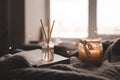 Bamboo sticks in bottle with scented candles and open book on wooden tray in bed closeup. Royalty Free Stock Photo