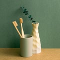 Bamboo toothbrush in a cup and eucalyptus leaf on brown shelf. green wall background. bathroom interior Royalty Free Stock Photo