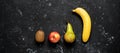 Banana apple kiwi and pear in a row on a black stone grunge background. Fresh fruits banner. Top view flat lay