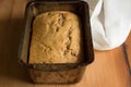 Banana bread in loaf tin on rustic wooden table with dish towel Royalty Free Stock Photo