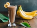 Banana-chocolate smoothie with cocoa, in a tall glass, on a wooden table. Healthy drink, vegetarian