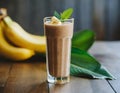 Banana-chocolate smoothie with cocoa, in a tall glass, on a wooden table. Healthy drink, vegetarian