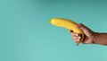 Banana Concept image. Hand Holding a Banana against the blue background, Look like a Gun. Metaphor Photo