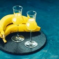 Banana flavoured liqueurs, which French call creme de banana, in grappas wineglass on dark blue concrete surface. European