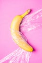Banana fruit wrapped in stretch wrap plastic on pink background, minimalistic creative layout