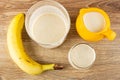 Banana, glass with blend from banana and milk, pitcher with milk, glass of dairy cocktail on table. Top view