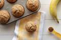 Banana Nut Muffins in Muffin Tray with Banana, Cinnamon, and Kitchen Towel on White Wood Background Royalty Free Stock Photo