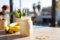 banana and oatmeal smoothie in a glass bottle jar and bananas on a white kitchen table. sunny blurred outside on background,