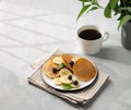 Banana pancakes with fresh fruit slices, berries, mint and honey on a light background with a cup of black coffee, shadows and Royalty Free Stock Photo