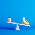 Banana sitting on seesaw with cupcake on opposite end on blue background