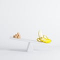 Banana sitting on seesaw with sugar cubes on opposite end on white background