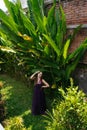 a banana tree growing up at a brick wall stands on the green grass of a girl in a long dress leaning against her head Royalty Free Stock Photo