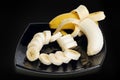 Banana whole and cutted slices on glass dish over black background