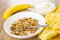 Bananas, bowl with yogurt, napkin, granola, spoon in plate on wooden table Royalty Free Stock Photo