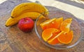 Bananas sliced oranges and red apple fruit on wooden table