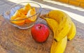Bananas sliced oranges and red apple fruit on wooden table