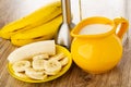 Bananas, transparent glass, electric blender, slices of banana in saucer, pitcher with milk on wooden table Royalty Free Stock Photo