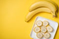 A banch of bananas and a sliced banana in a dish over yellow background. Royalty Free Stock Photo