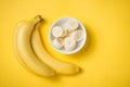 A banch of bananas and a sliced banana in a dish over yellow background. Royalty Free Stock Photo