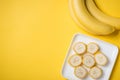 A banch of bananas and a sliced banana in a dish over yellow background. Royalty Free Stock Photo