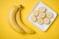 A banch of bananas and a sliced banana in a dish over yellow background. Royalty Free Stock Photo