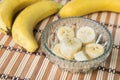 A banch of bananas and a sliced banana in a pot over a wood background