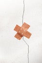 Band-aid plaster in cross shape on a crack in the wall, concept Royalty Free Stock Photo