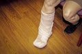 Bandaged foot and leg of cropped woman in shorts against wooden floor as she sits on bench or chair