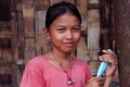 Portrait of a young tribal girl standing in front of a bamboo fence with a mask.