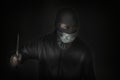 Bandit in black mask with a slit for the eyes and a medical mask waving a knife. Royalty Free Stock Photo