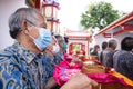 An Older man wearing a white mask while holding a tray and praying in pandemic