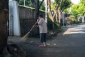 An unknown woman cleans the yard of the house using a broom.