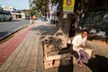 An Indian man sitting on a stone bench under a tree on a wide sidewalk in the city of Royalty Free Stock Photo