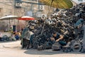 Street scrap yard worker with mountain of engine pieces surrounding him.