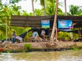 Cottage industry along river in Thailand conducted under lightweight shelter with colourful signs