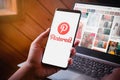 Bangkok, Thailand - August 6, 2019: Hands holding Smartphone with Pinterest logo screen and Pinterest website on laptop background