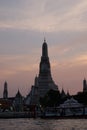 Sunset over the Wat Arun Buddhist Temple. A small passenger ferry at the pier of the Chao