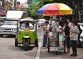 Bangkok Thailand. Green auto rickshaw Tuk Tuk with driver in traffic with cars and people eating on street food st