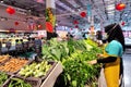 Bangkok, Thailand - January 17, 2023 : asian muslim woman working as shop assistant and restocking fresh organic vegetables into Royalty Free Stock Photo