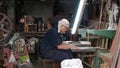 BANGKOK, THAILAND - 11 JULY, 2019: Ethnic craftsman working in street workshop. Side view of male artisan sitting near workbench