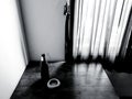 Bottle of beer and ceramic astray putting on wooden table with red curtain and sunlight from window in black and white tone