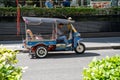 Tuk Tuk taxi cab driver waits for passengers, using his cell phone while parked on the side