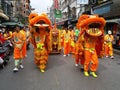 Two dancing lions in front of a group of people carrying a cart with percussion in the parade of a Festival of the Clans of the C