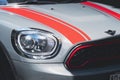 Close up of headlight with red stripes on bonnet surface of Bronze MINI COOPER S COUNTRYMAN car in outdoor parking area