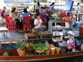 People eating at a table while a woman cooks in a boat at the Taling Chan Floating Market in Bangkok